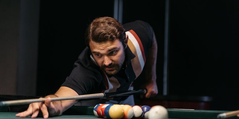 Man concentrating on a shot leaning over pool table with cue stick
