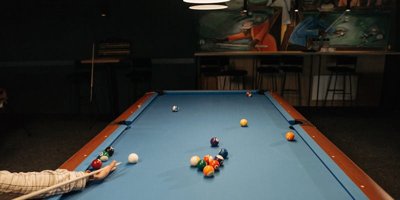 Person holding a cue stick preparing to shoot at a pool table
