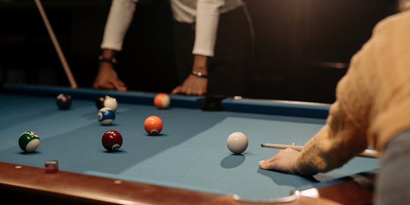 Two people playing pool with cue sticks over blue felt billiards table
