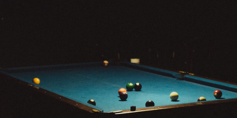 Pool table with billiard balls on blue felt in a dimly lit bar