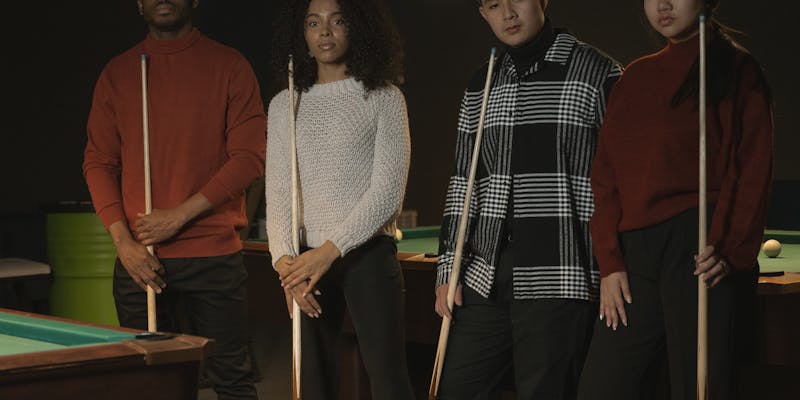 Four billiard players standing together holding cue sticks
